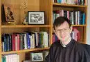 Fr Sam Tanna-Korn in his study in front of bookcases and a crucifix