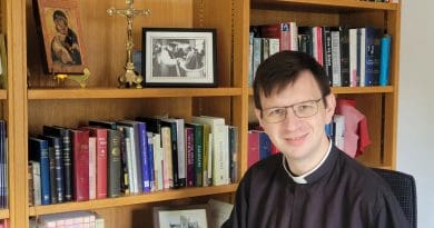 Fr Sam Tanna-Korn in his study in front of bookcases and a crucifix