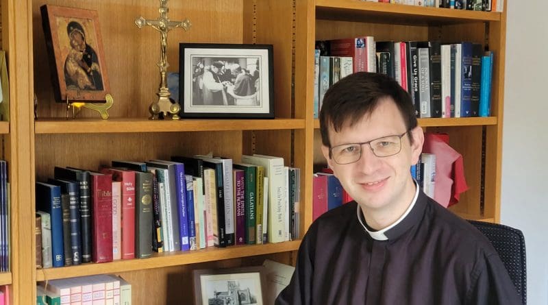 Fr Sam Tanna-Korn in his study in front of bookcases and a crucifix